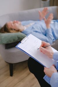 Therapist taking notes while a patient lies on the couch during a therapy session.